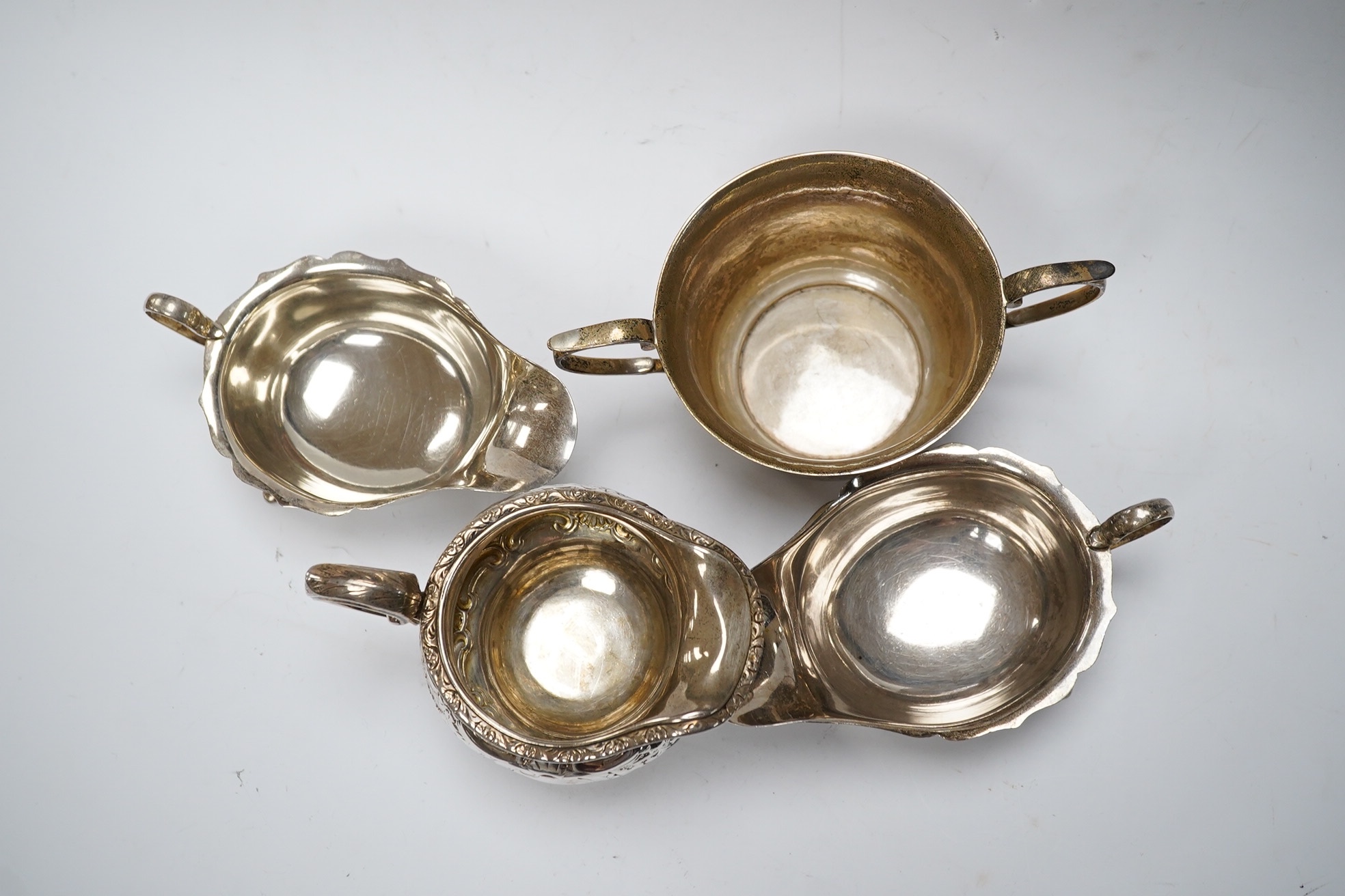 A George III Scottish silver cream jug, later embossed, a pair of George V silver sauce boats and an Edwardian hammered silver two handled porringer, by Moss Morris,18.4oz. Condition - poor to fair